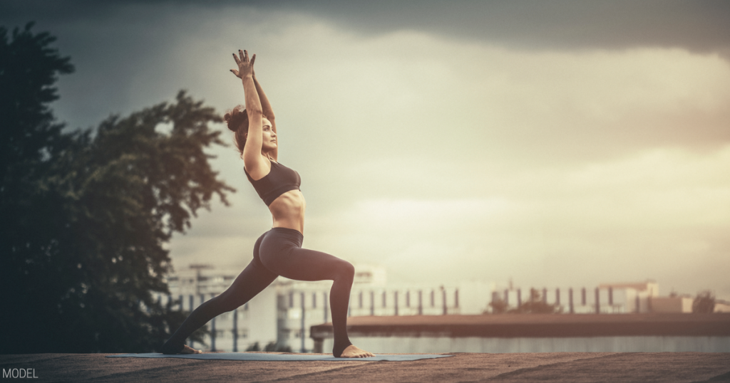 Woman doing the warrior 1 yoga pose outside by the waterfront