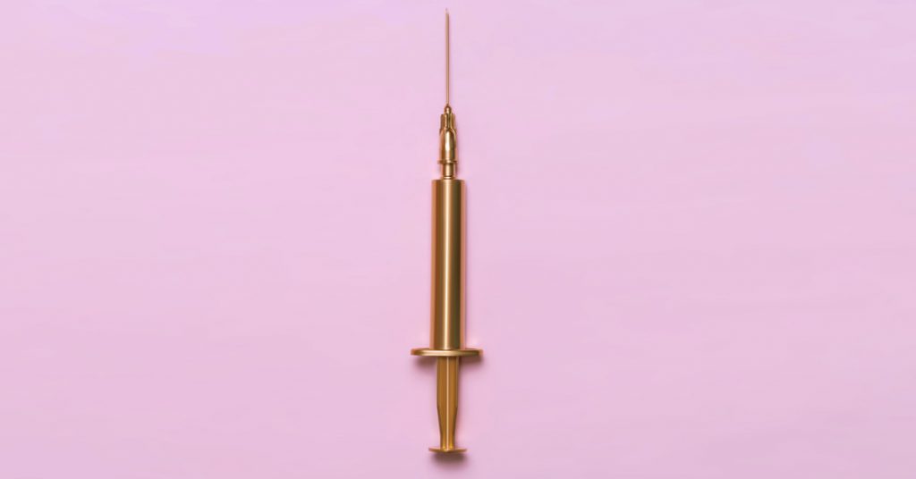 Gold syringe on pink background