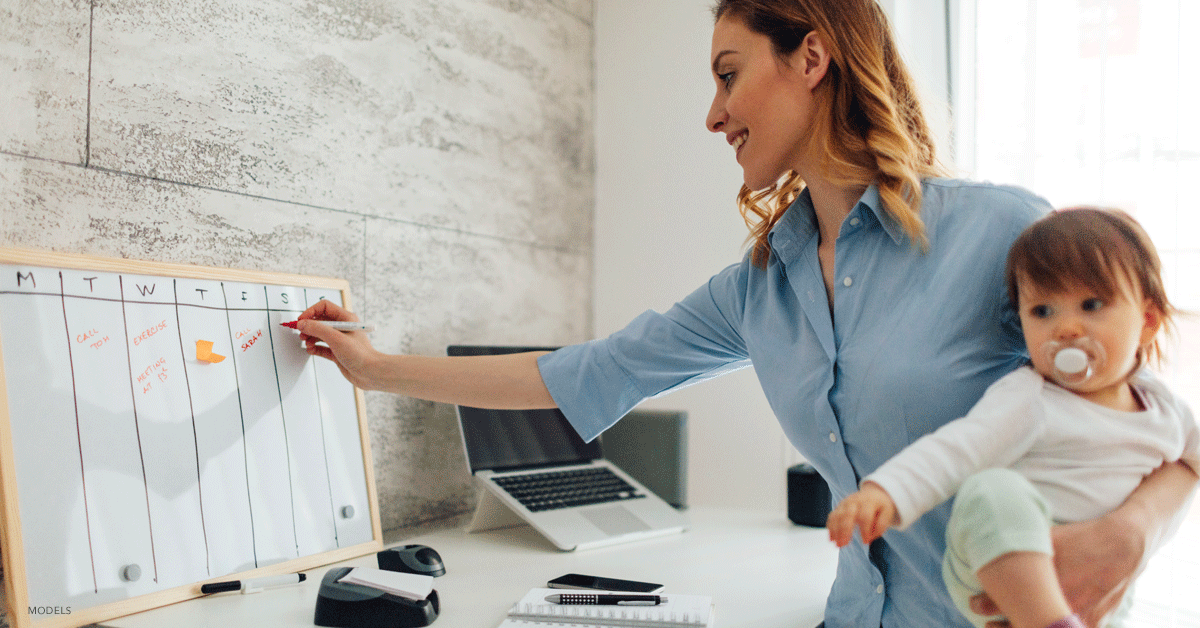 Busy mom holding her baby looking at calendar for a time to schedule a CoolSculpting® treatment.