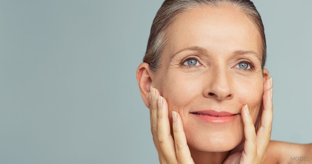 Beautiful middle-aged woman holding her face and smiling. (Model)