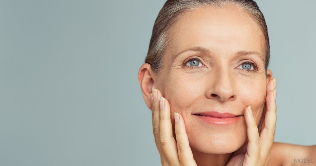 Beautiful middle aged woman smiling while holding her smooth face. (Model)
