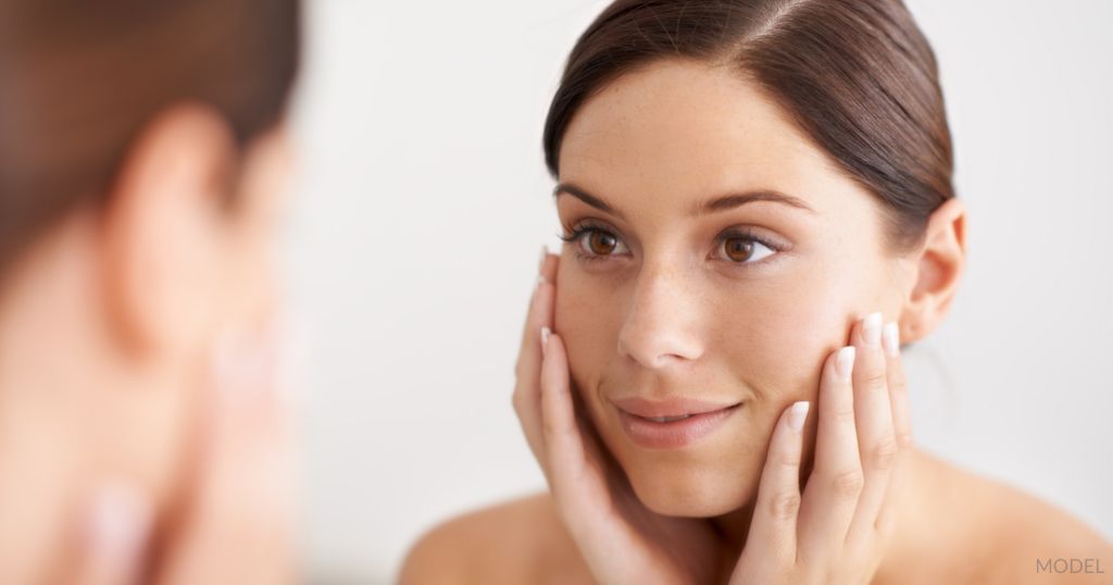 Beautiful woman admiring her smooth skin in mirror reflection. (Model)