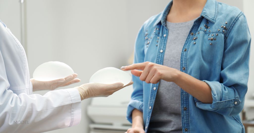 A doctor holding out breast implants to a woman to examine. (Model)