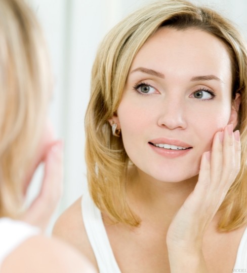A woman looking at their face in the mirror. (MODEL)
