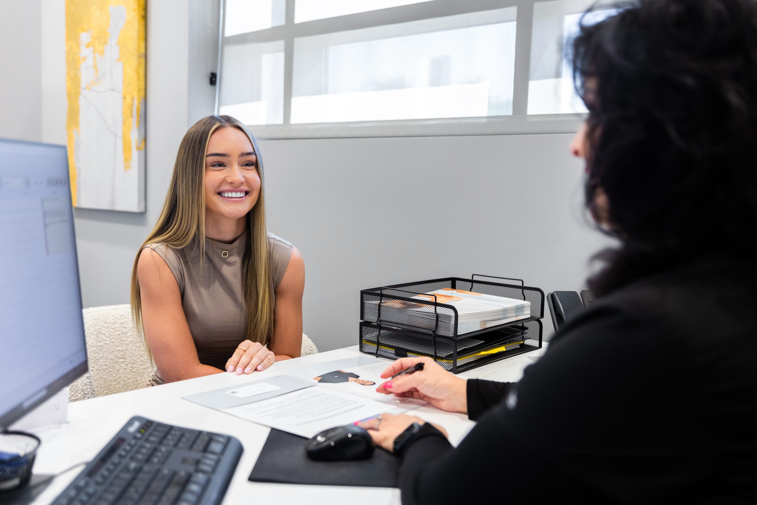 Smiling woman sitting across a desk from an Advanced Skin Lounge employee